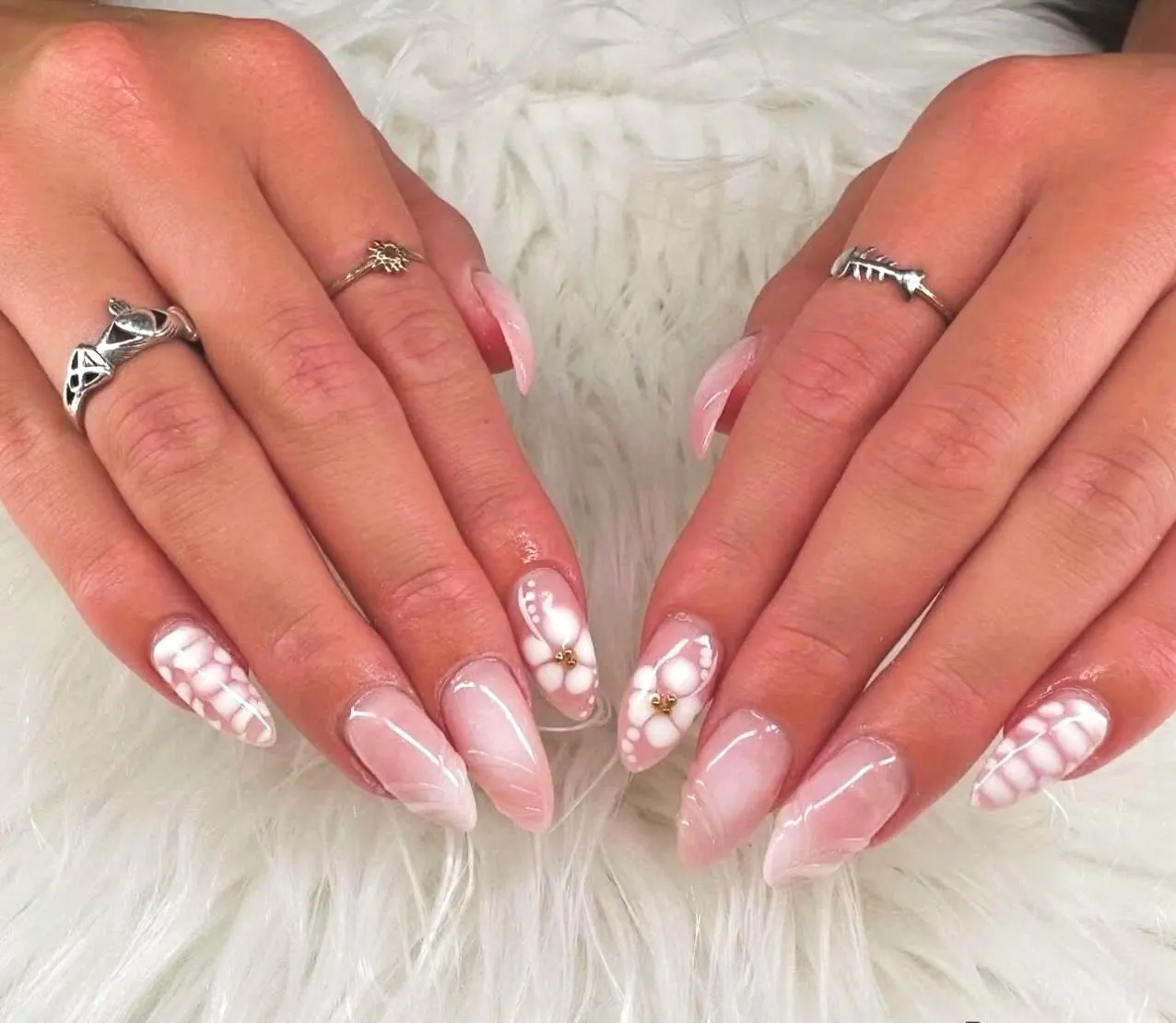 Milky pink almond nails with white hand-painted flowers, done at Onyx