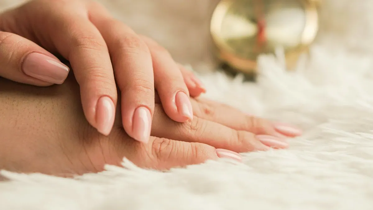 Soft nude almond manicure resting on ivory faux fur